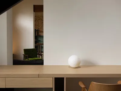 Modern home office featuring a minimalist wooden desk with a white spherical object and a retro green chair, against white wa