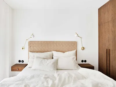 Minimalist bedroom featuring a woven headboard, white linen bedding, and wooden nightstands with wall-mounted lamps.