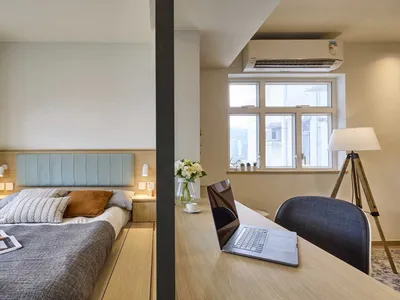 A modern minimalist bedroom featuring a wooden bed frame, wall-mounted lights, and a window with a view.