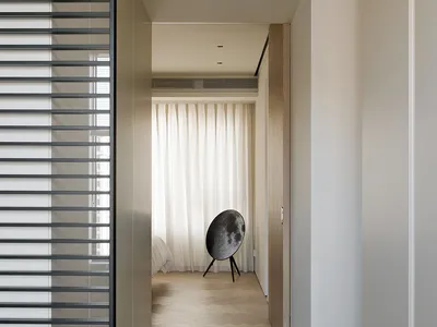 Modern minimalist bedroom featuring wooden flooring and white curtains, viewed from a hallway perspective.