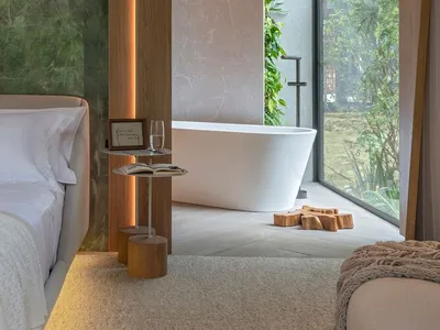 A minimalist bedroom with a marble wall, wooden accents, and a large window overlooking trees.