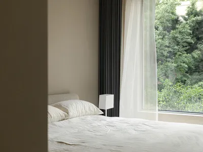 A minimalist bedroom with a bed featuring white textiles and natural light streaming through a large window with a sheer curt