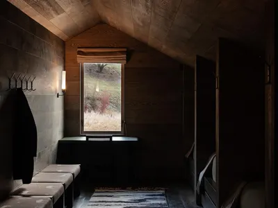 Modern minimalist bedroom with wood paneling, a window with natural light, and a cozy sitting area.