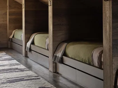 A minimalist bedroom featuring wooden walls and floors, with three single beds in a slanted room.