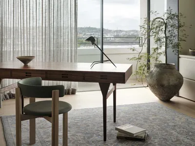 A modern home office with a wooden desk, green chair, and large window overlooking a city.