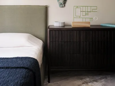 A minimalist bedroom featuring wooden furniture, a green headboard, and a side table with decorative items.