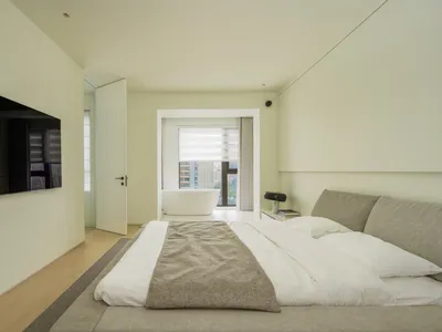 Modern minimalist bedroom featuring a bed with a fabric headboard, wooden floor, and glass window