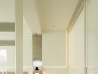 Modern minimalist bedroom with white walls, wooden flooring, and simple furniture arrangement.