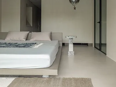Minimalist bedroom featuring a concrete platform bed with a textured rug and a contemporary pendant light hanging above it.