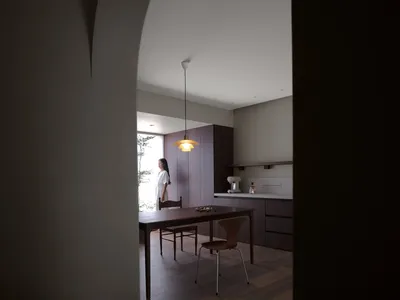 簡約住宅廚房，搭配木質地板與櫥櫃，配有現代吊燈，一位女性站立其中