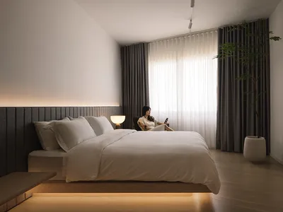 簡約臥室內設有木質紋理床頭板與地板、白色的床具，以及角落的一盆盆栽