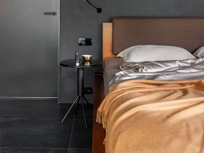 A minimalist bedroom featuring a bed with a brown upholstered headboard, a yellow blanket, and a black side table with a lamp