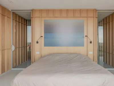 A minimalist bedroom with wood paneled walls and a gray bedspread.