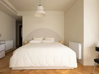 A minimalist bedroom with a bed dressed in neutral-colored bedding and a curved headboard.