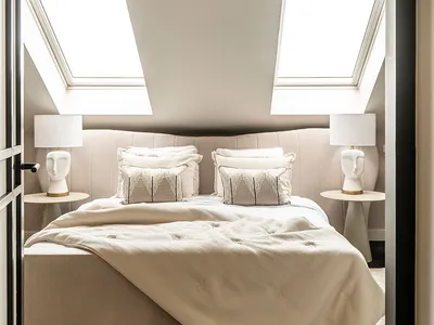 Modern, minimalist bedroom with white bedding, pillows, and a light-colored fabric headboard, featuring skylights and a cozy