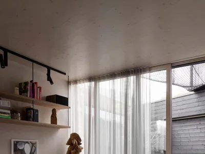 A living room with a brown leather sectional sofa, glass coffee table, wooden floor, and large windows with sheer curtains.