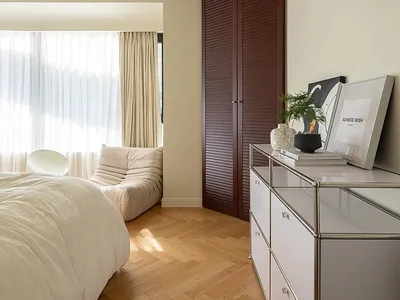 A minimalist bedroom with white furniture and wood flooring.