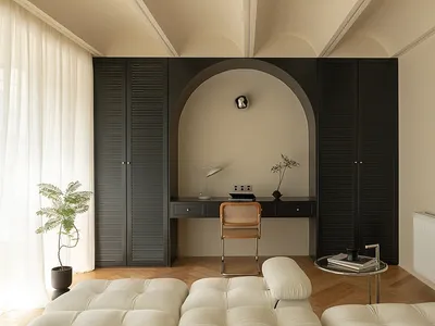A minimalist home office featuring a sleek black desk with a white cushioned bench and a small potted plant.