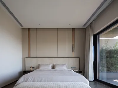 Modern minimalist bedroom featuring neutral-toned furniture and decor, clean lines, and a large window.