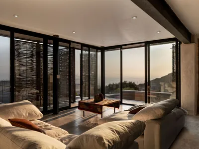 A modern, minimalist living room with concrete surfaces, natural light, and ocean views.