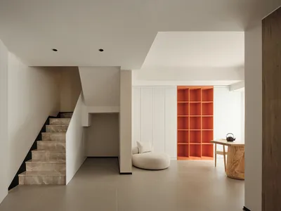 Modern minimalist living room featuring concrete flooring, white walls, and orange shelving.