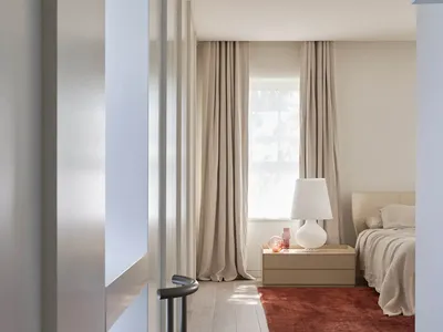 A minimalist bedroom with wooden flooring, a bed, a side table with a lamp, and a green chair against the wall.