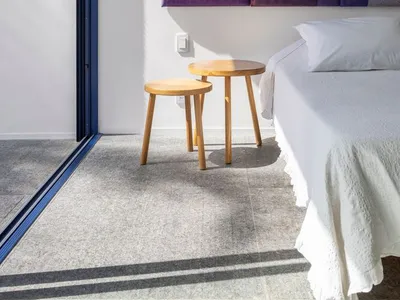 A modern bedroom featuring a bed with gray bedding, wooden stools, and a wall art piece with purple and brown panels.