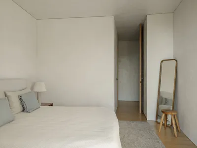A minimalist bedroom with a bed, lamp, mirror, stool, and rug.