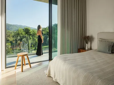 A modern bedroom with a glass door providing a view of greenery outside, featuring a canvas window treatment and a single woo