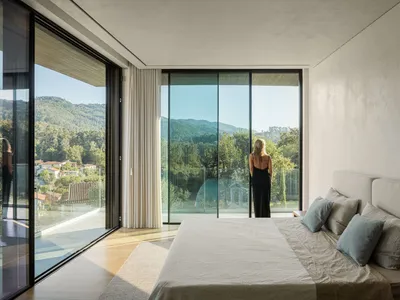 A modern bedroom with large glass windows overlooking green hills.