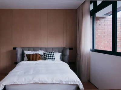 A minimalist bedroom featuring a bed with wooden headboard and white bedding, surrounded by wooden panels.