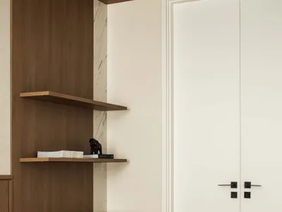 A minimalist bedroom with a white bed, wooden shelves, marble accent wall, and black stool.