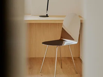 A modern home office featuring a sleek, minimalist desk made of light wood with a black adjustable desk lamp and a modern met
