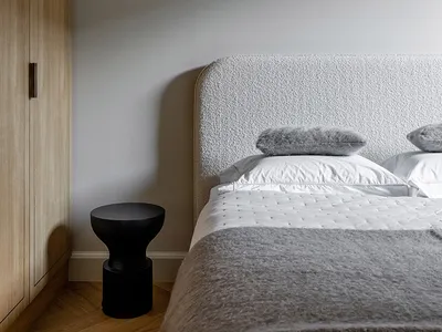 A minimalist bedroom featuring a grey upholstered bed, grey pillows, and a black side table.