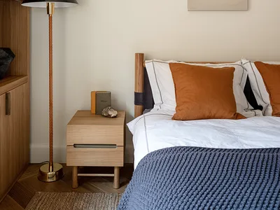 A modern minimalist bedroom with wooden furniture, a floor lamp, and a bed with white sheets and orange pillows.