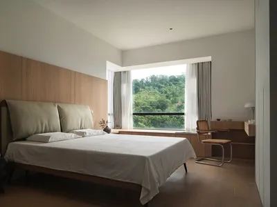 A minimalist bedroom featuring a bed with a wooden headboard and white bedding, surrounded by modern furniture and a large wi