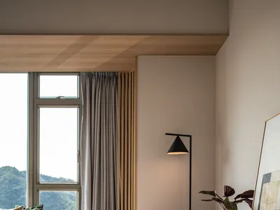 A minimalist bedroom with a wooden armchair, floor lamp, and dresser.