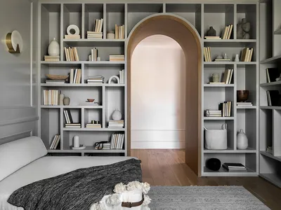 A modern minimalist bedroom with shelves filled with books and decorative items, featuring a bed with white and grey bedding,