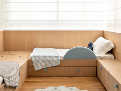 A minimalist bedroom featuring wooden beds with built-in storage and soft textiles.