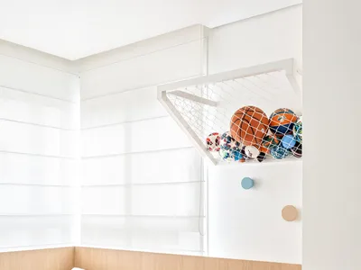 A modern minimalist children's bedroom featuring a bed with a blue headboard, built-in storage units, and a net holding sport