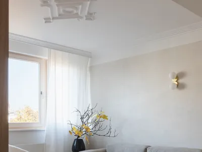 Modern minimalist living room with a light grey sofa, white armchair, and a marble side table with a plant.