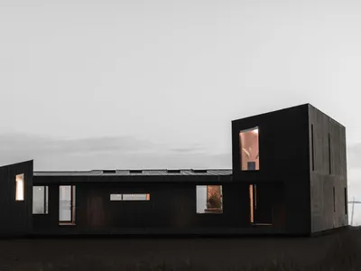 A modern house exterior with a minimalist design and black painted walls, featuring large windows and a simple geometric shap