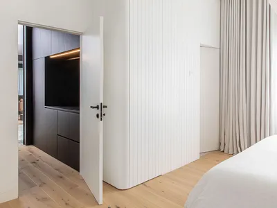 A modern minimalist bedroom featuring white accent wall and wooden flooring.