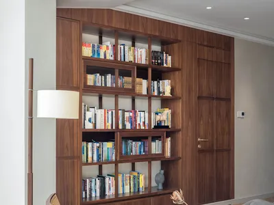 A living room with industrial-style decor, featuring wooden shelves filled with books and a wooden armchair on a rug.