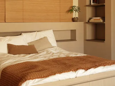 A minimalist bedroom with wooden bed platform, bamboo headboard, and fabric bedding and throw blanket.