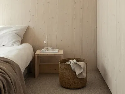 A minimalist bedroom featuring wooden walls and a wooden nightstand with a glass decanter and two glasses.