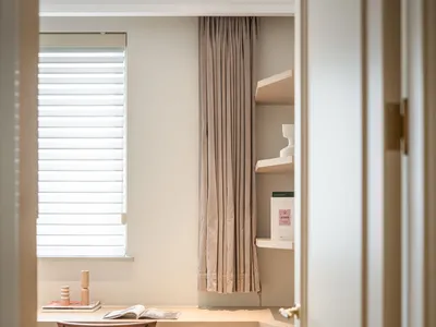 A modern home office featuring wooden furniture, a window with blinds, and a bookshelf.
