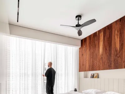 A minimalist bedroom featuring white bedding, a wooden headboard, and sheer curtains allowing sunlight to filter through.