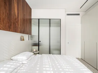 A minimalist bedroom featuring glass walls and a white bed with wooden accents.