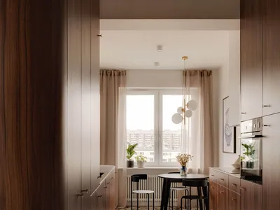 A minimalist residential kitchen with wooden cabinets and a tiled floor, featuring a dining area with chairs and a round tabl